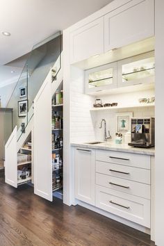 an open kitchen with white cabinets and wooden flooring in the center, along with stairs leading up to the upper level