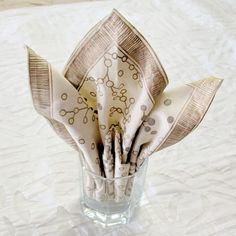 folded napkins in a clear glass on a white tableclothed surface with circles and dots