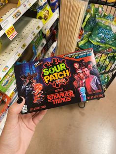 a person holding up a card game in a store aisle with other items on the shelves