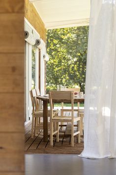 a wooden table and chairs sitting on top of a porch next to a white curtain