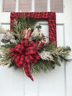 a red and black plaid wreath hanging on the front door with pine cones, evergreens and other greenery