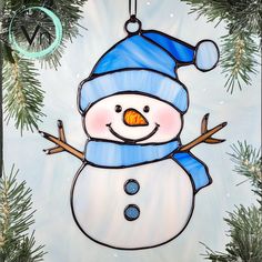 a stained glass snowman ornament hanging from a christmas tree with pine needles