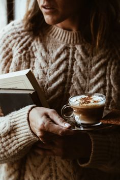 a woman is holding a book and a cup of cappuccino in her hands