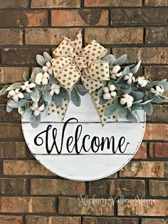 a welcome sign hanging on the side of a brick wall with greenery and bows