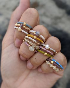 a person is holding several rings in their hand with beads and stones on them,