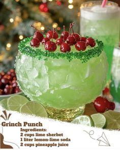 a green drink with cherries and limes on the rim next to a christmas tree