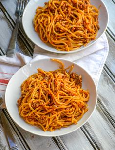 two white plates filled with spaghetti on top of a wooden table