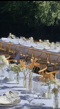 a long table is set up with flowers and place settings for an outdoor wedding reception