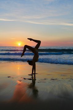 a woman doing a handstand on the beach at sunset with her arms in the air