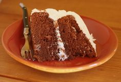 a slice of chocolate cake with white frosting on a plate next to a fork