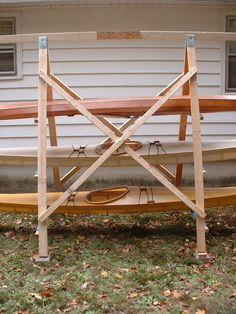 a boat sitting on top of a wooden stand in front of a house with two kayaks attached to it