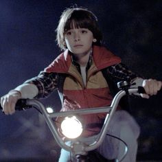 a young boy riding on the handle bars of a motorcycle at night with his headlight on