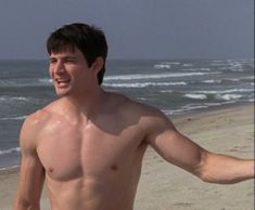 a shirtless man walking on the beach with his arms out to the side, holding a frisbee in one hand