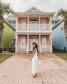 a woman standing in front of a multi - colored house wearing a straw hat and white dress