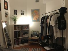 a bedroom with clothes hanging on the rack and bookshelf in front of it