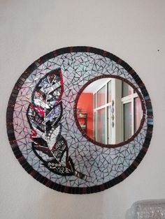 a round mirror hanging on the side of a wall next to a vase and door