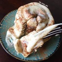 a blue plate topped with cinnamon rolls covered in icing next to a knife and fork