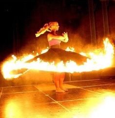 a woman standing on top of a dance floor with fire in the air behind her