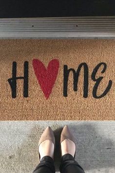 a person standing in front of a door mat with the word home painted on it