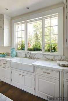 a large kitchen with white cabinets and marble counter tops is pictured in this image, there are two windows above the sink