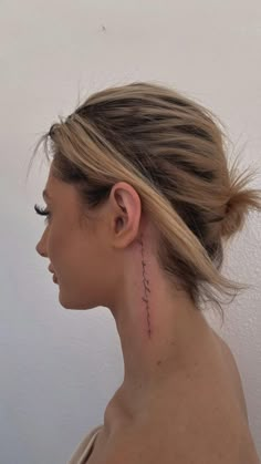 a woman with a small tattoo on her neck and behind her ear, looking to the side