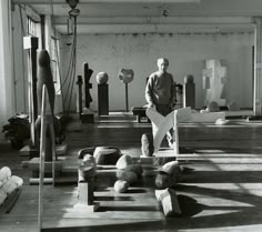 a black and white photo of a man standing in an art gallery surrounded by sculptures