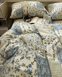 an unmade bed with blue and white flowers on the comforter, next to a night stand