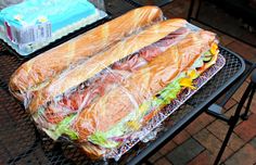 two large sandwiches wrapped in plastic sitting on top of a metal grill grate next to a bag of ice cream