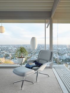 an eames chair and ottoman in front of a large window overlooking the city