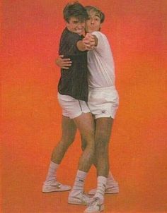 two young men hugging each other while standing on a tennis court in front of an orange background