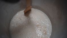 a bowl filled with white liquid being stirred by a wooden spoon on top of it