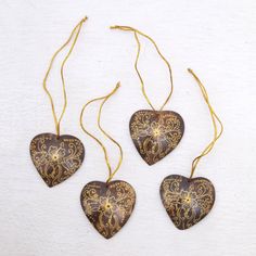 three heart shaped ornaments hanging from strings on a white surface with gold thread and beads