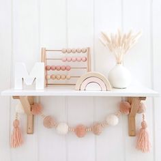 a white shelf topped with pink and white decorations next to a wooden letter m on top of a wall