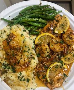 a white plate topped with shrimp, mashed potatoes and lemon wedged green beans