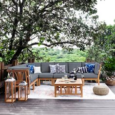 an outdoor living area with couches, tables and plants on the deck overlooking trees