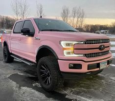 a pink truck is parked in the parking lot with snow on the ground and trees behind it