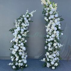 two white flowers and greenery are arranged in the shape of an arch