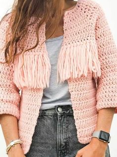 a woman wearing a pink crocheted jacket with fringes