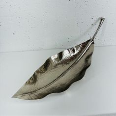 a silver leaf shaped tray with handles on a white surface, and water droplets all around it