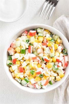 a white bowl filled with corn salad next to a fork and napkin on top of a table