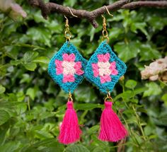 crocheted earrings with pink and blue tassels hanging from a tree branch