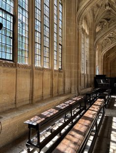 the sun shines through two windows in an old building with long benches and piano