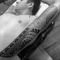 a man laying on top of a wooden floor next to a wall with tattoos on his arm