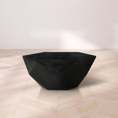 a black bowl sitting on top of a hard wood floor next to a white wall