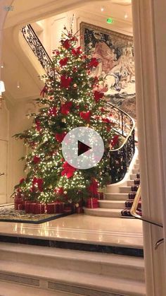 a christmas tree in the middle of a room with stairs and chandelier above it