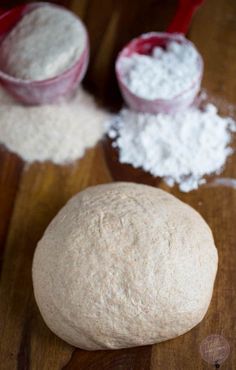 a ball of bread sitting on top of a wooden table next to two measuring cups