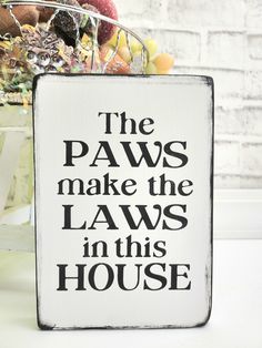 a sign that says the paws make the laws in this house with fruit behind it