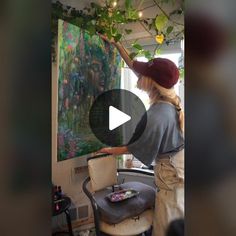 a woman in a red hat is painting on a wall with green plants and lights