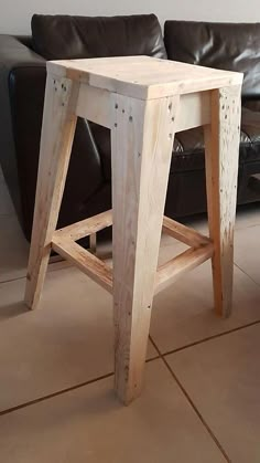 a wooden stool sitting on top of a tile floor next to a leather couch in a living room