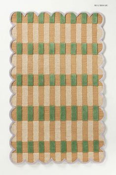 a green and beige checkered rug with scalloped edges on a white background